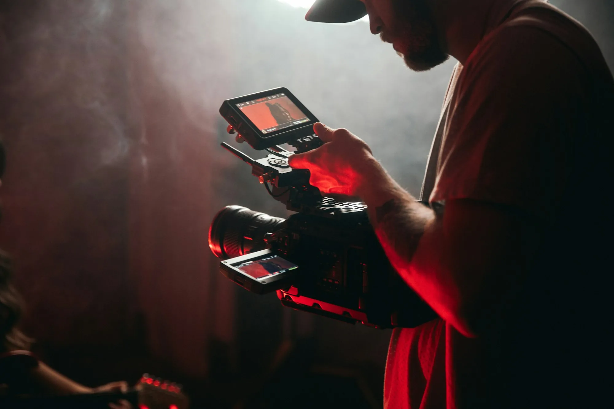 Camera operator framing a shot on a cinema camera under deep red lighting