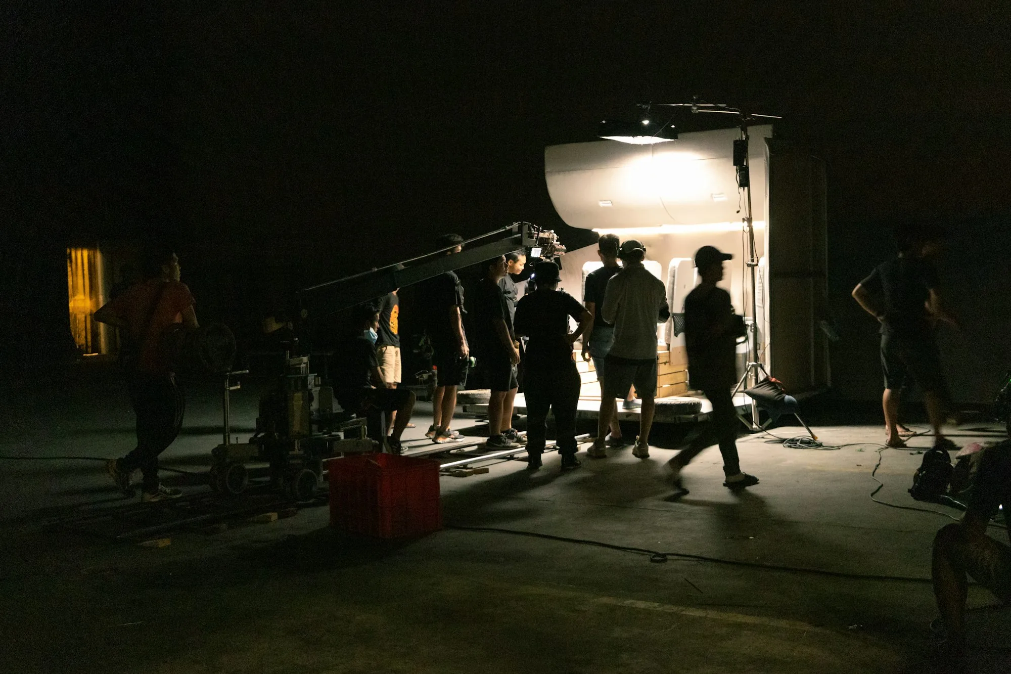 A film crew at work on a lit night set, cinema camera and lighting rigs in silhouette