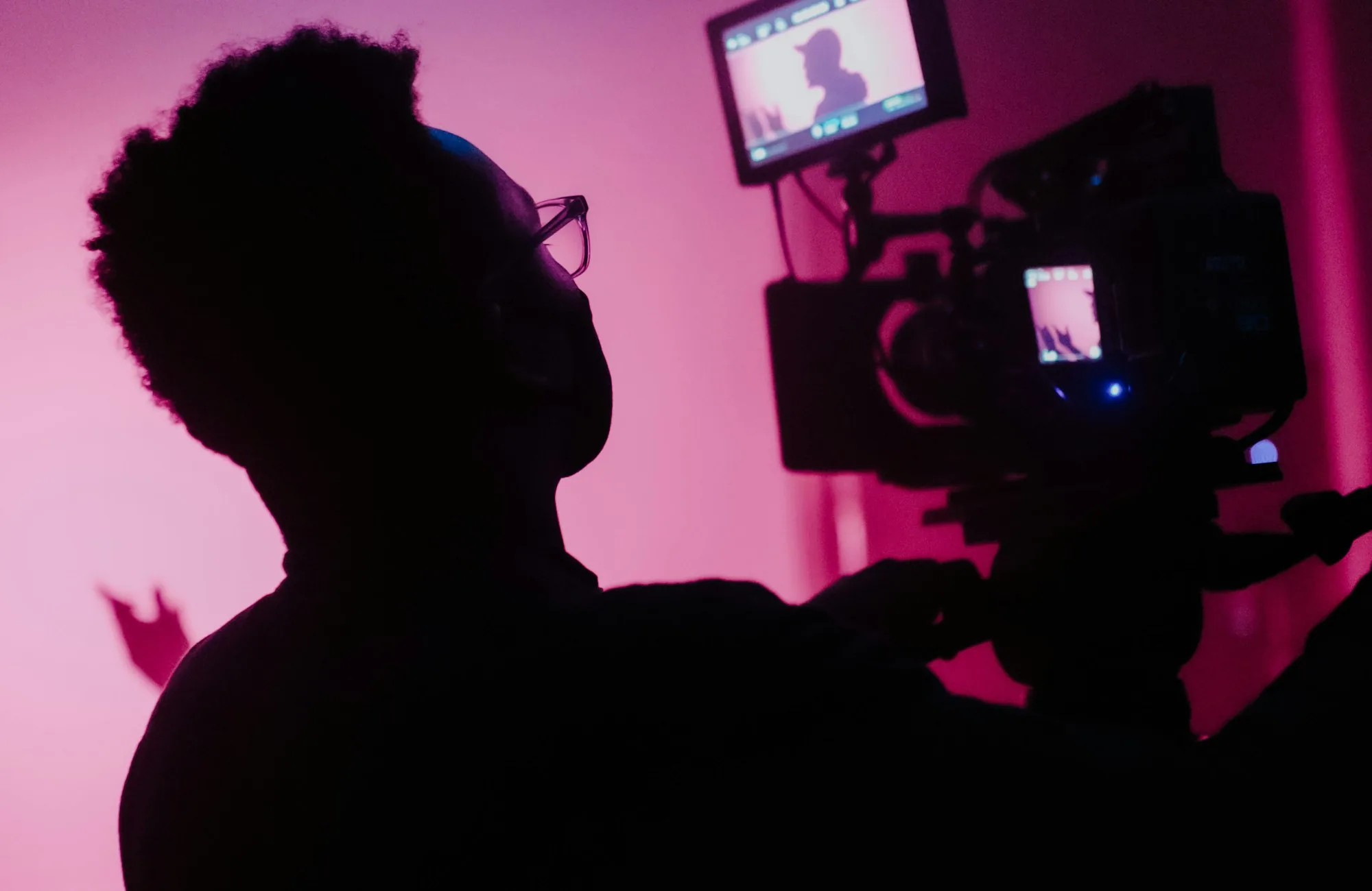 A director silhouetted against production monitors on a lit sound stage